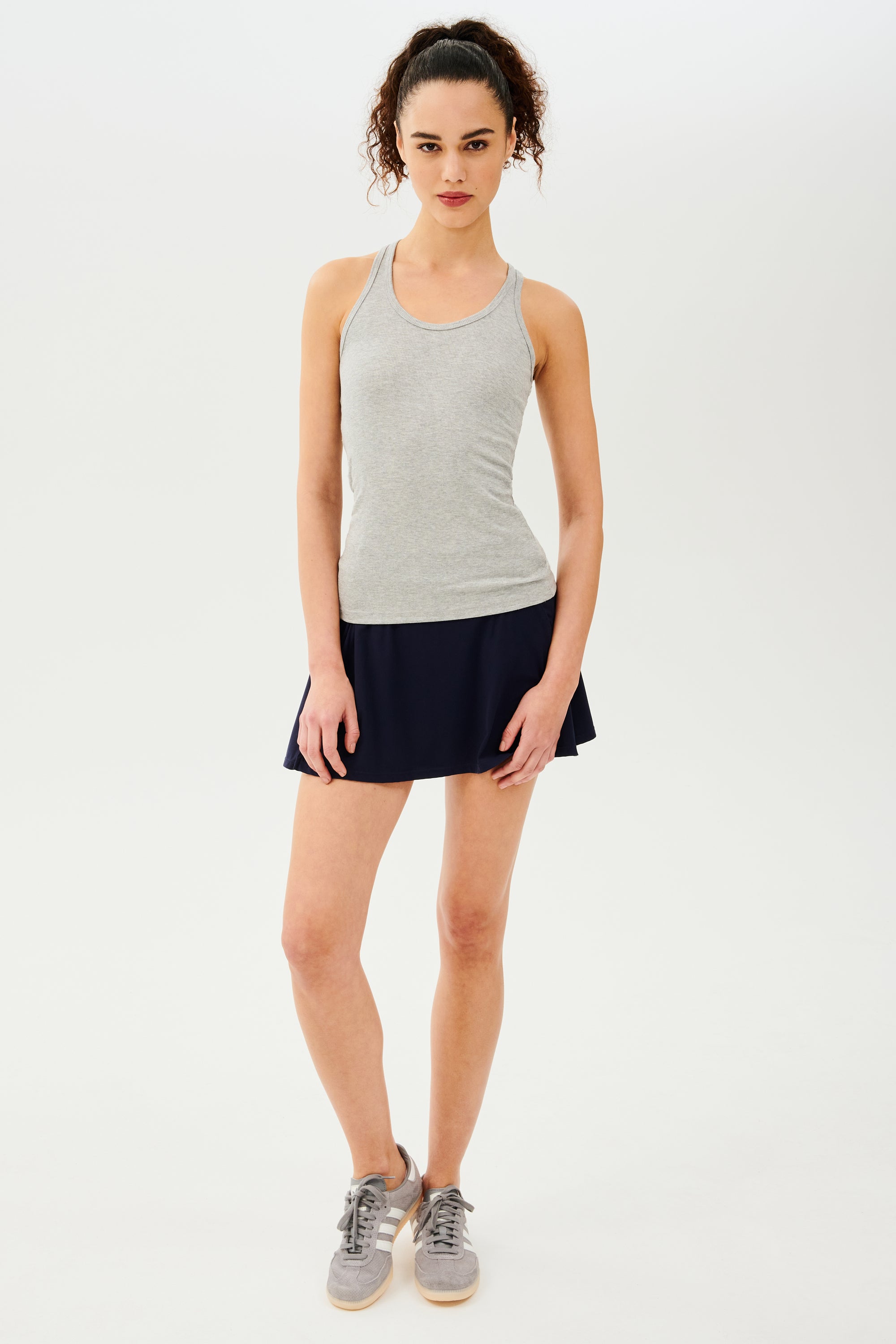 Front view of girl wearing a light grey tank top and black skirt with grey shoes