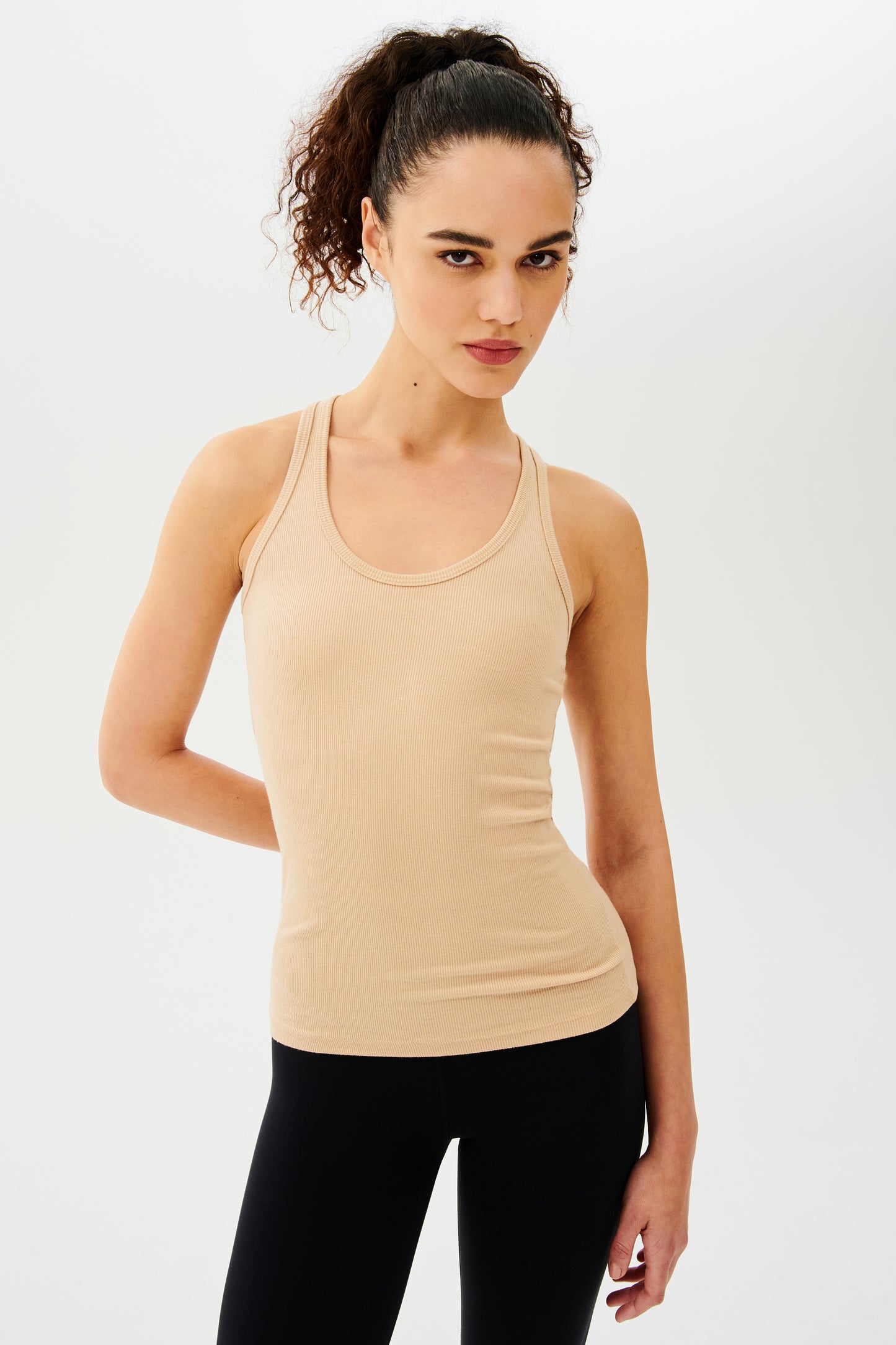 Front view of girl wearing a yellowish brown ribbed tank top and black leggings with white shoes
