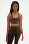 Front view of woman with black braids wearing dark brown bra and dark brown leggings